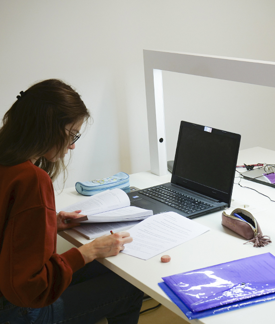 Estudiante con apuntes y un ordenador portátil en una mesa de estudio de la bilbioteca de derecho