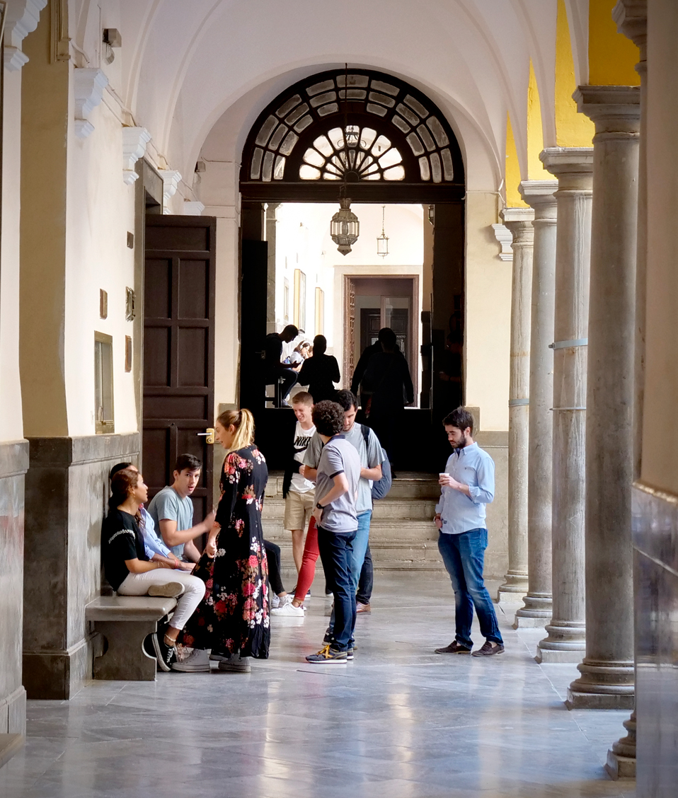 Imagen de uno de los pasillos de la Facultad de Derecho, en ella, varios estudiantes se encuentran transitando o sentados en algunos de sus bancos