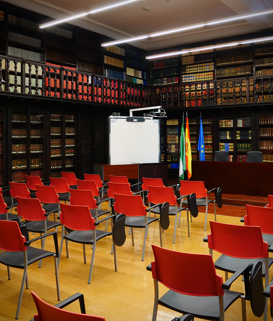 Sala de conferencias de la Facultad de Derecho. El espacio se encuentra rodeado de estanterías repletas de libros y cuenta con sillas para los asistentes y proyector